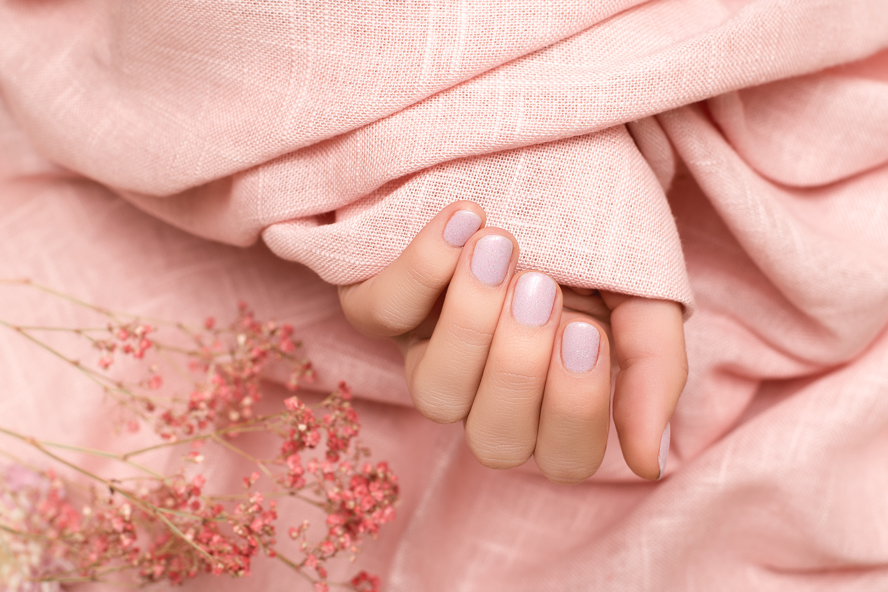 Female hand with pink nail design. Pink nail polish manicure. Woman hand hold pink fabric.